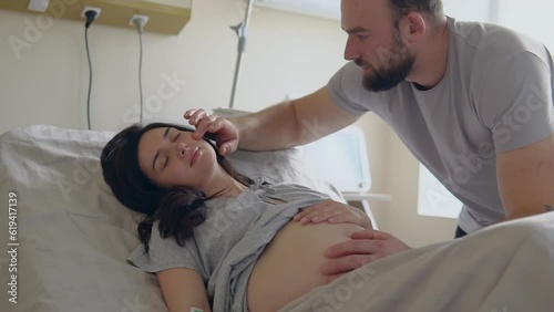 Caring husband touching tummy and adjusting hair of pregnant wife during childbirth photo