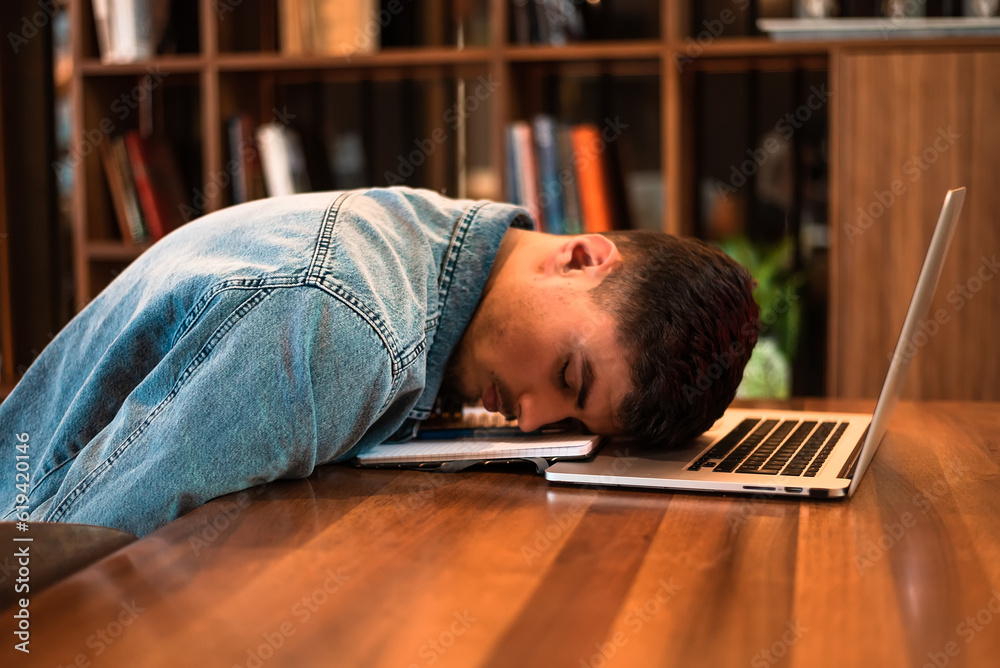 A tired student sleeping on the table inside university library. A tired student sleeping on the table inside university library.