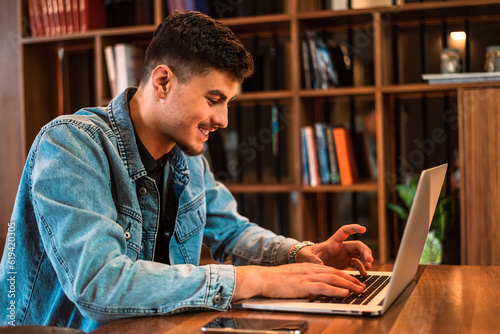 A happy male college student using a laptop in a university library.