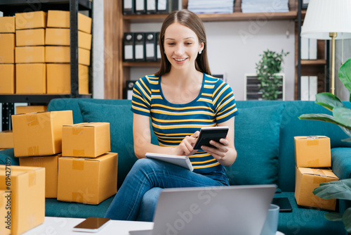 Entrepreneur using calculator with pencil in her hand, calculating financial expense at home office, online market packing box delivery,Startup successful small business owner, SME, concept.