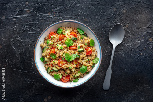 Quinoa tabbouleh salad in a bowl, a healthy dinner with tomatoes and mint, overhead shot with a spoon photo