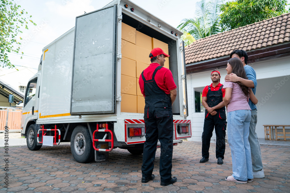 Fototapeta premium Wide shot of two delivery man opern truck door and show to couple people as customer at the house and they look happy.