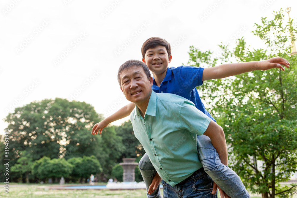 asian boy flying forward on dad's back in summer, korean senior pensioner playing with child in summer outdoors