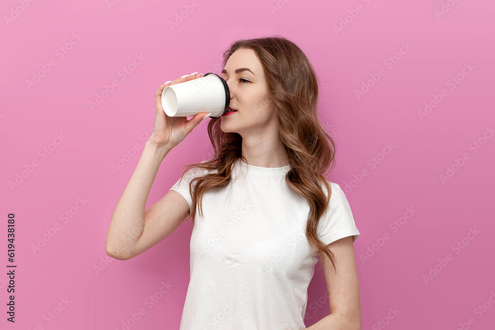 cute woman drinks coffee from paper cup on pink isolated background, girl in white t-shirt drinks drink cute woman drinks coffee from paper cup on pink isolated background, girl in white t-shirt drinks drink