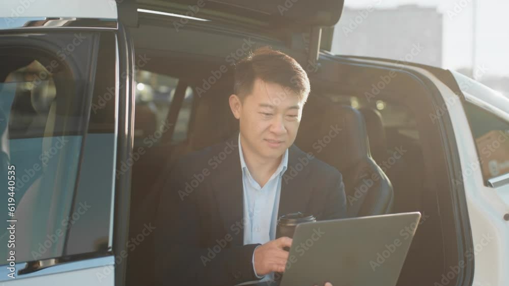 Astylish asian entrepreneur using wireless laptop while charging electric car on public station. Modern technology for distance work and ecological transport for lifestyles. Charging electric car. Astylish asian entrepreneur using wireless laptop while charging electric car on public station. Modern technology for distance work and ecological transport for lifestyles. Charging electric car.
