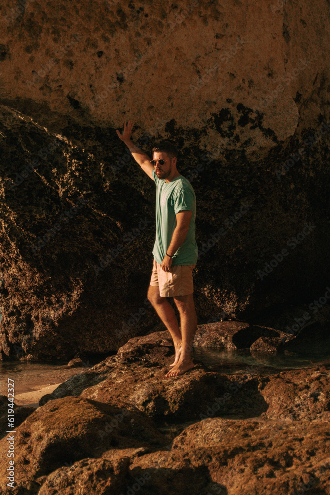 Podróżnik o zachodzie słońca na tle oceanu stojący przy skałach. - obrazy, fototapety, plakaty 