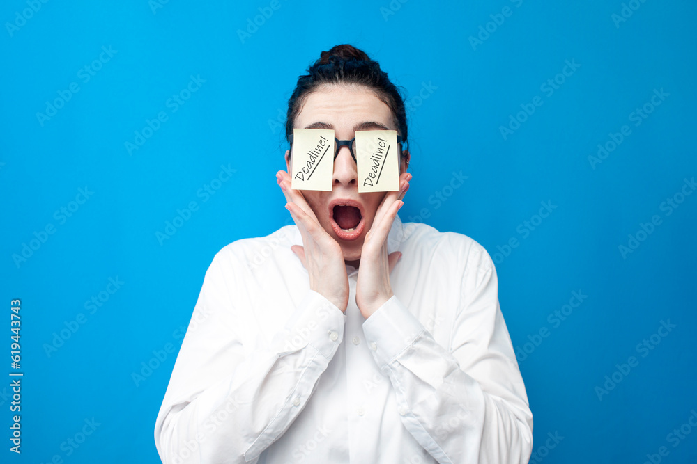 shocked woman manager screaming on blue background, girl office worker with papers in front of her eyes surprised