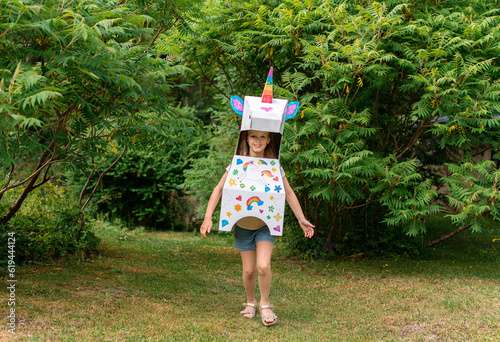 Little caucasian girl in unicorn paper costume outdoor funny playing, sunny summer day. Holiday concept, summer time