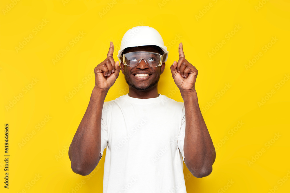 joyful male african american builder in uniform smiles and shows with his hand up on yellow isolated background