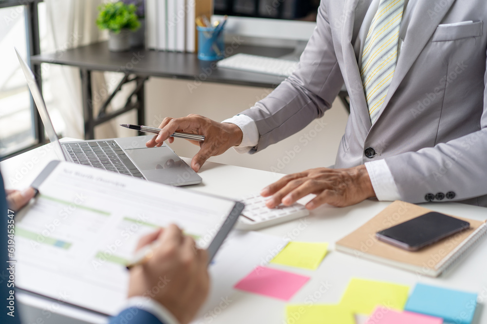 Businessmen use a calculator to calculate company financial statements for their colleagues, view and jointly solve problems within the company. Business finance and accounting concepts Businessmen use a calculator to calculate company financial statements for their colleagues, view and jointly solve problems within the company. Business finance and accounting concepts