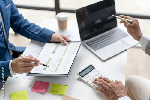 Group of business people meeting to plan, think, analyze, point to graph and business growth to plan new business expansion in the future using a laptop and a calculator.