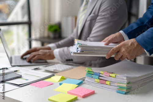 Businessman man working in stacks of papers searching for unfinished paperwork information on form check stack on table and checking financial papers in busy workload