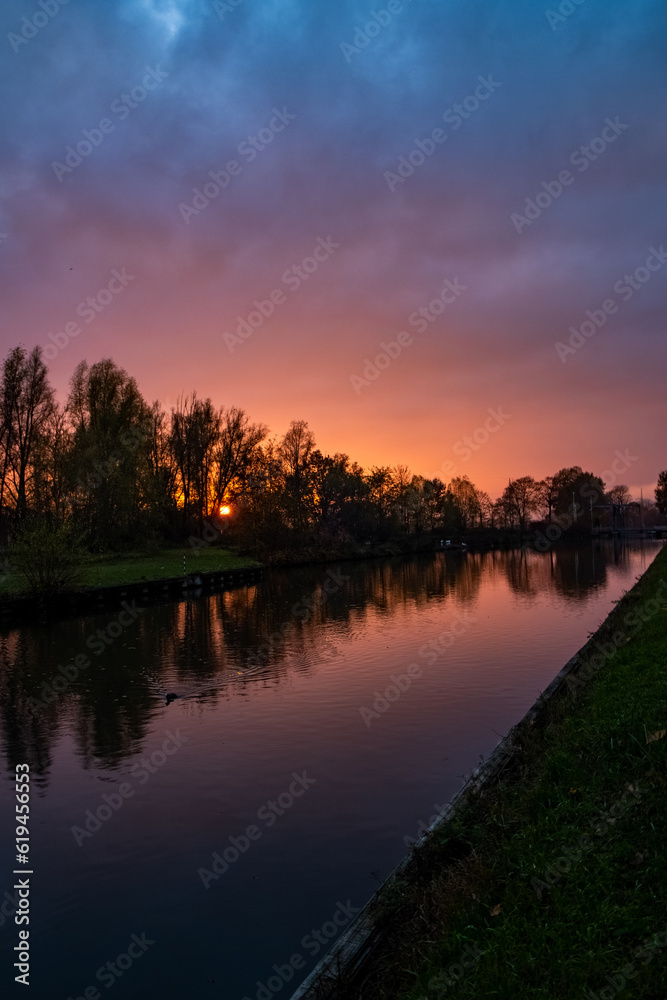 Witness the awe-inspiring beauty of nature's masterpiece as a dramatic and colorful sunset sky paints a breathtaking canvas, with tree silhouettes reflected in the calm waters of the river. The sky Witness the awe-inspiring beauty of nature's masterpiece as a dramatic and colorful sunset sky paints a breathtaking canvas, with tree silhouettes reflected in the calm waters of the river. The sky