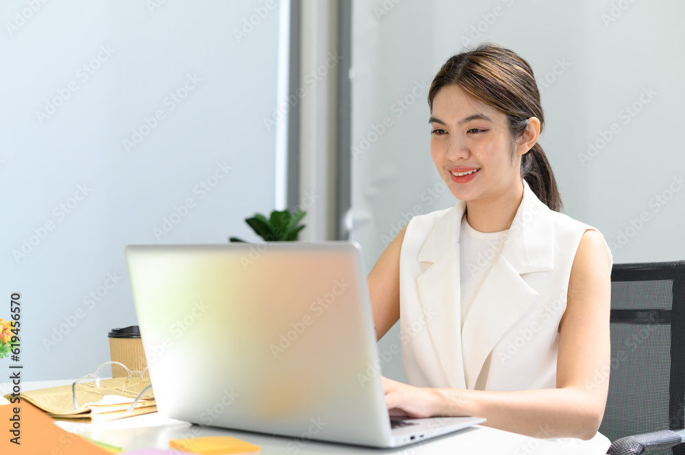 businesswoman sitting at the table while busy working on laptop computer at the office. Woman typing document, checking email, and participating in online meetings at workplace. businesswoman sitting at the table while busy working on laptop computer at the office. Woman typing document, checking email, and participating in online meetings at workplace.