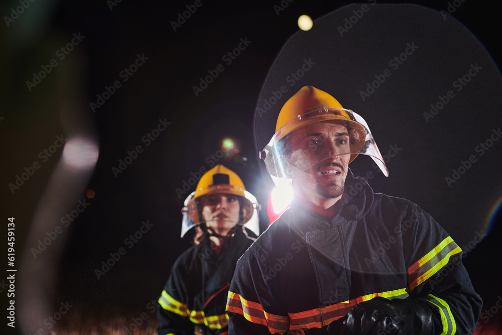 Fototapeta premium Firefighters using a water hose to eliminate a fire hazard. Team of female and male firemen in dangerous rescue mission. 