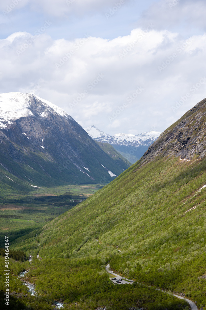 Norwegian mountain Trollstigen, on an early spring day when there is snow on the mountain and the rocks are gray but above them is a blue sky with white clouds and green grass Norwegian mountain Trollstigen, on an early spring day when there is snow on the mountain and the rocks are gray but above them is a blue sky with white clouds and green grass