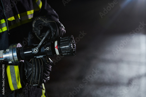 Firefighter using a water hose to eliminate a fire hazard. Team of firemen in the dangerous rescue mission.