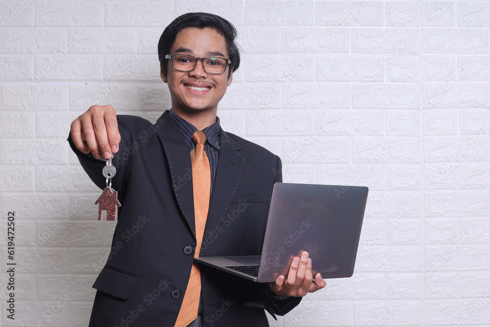Successful young businessman real estate broker holding laptop, showing key of a new house with smiling. Business, eco, real estate and office concept Successful young businessman real estate broker holding laptop, showing key of a new house with smiling. Business, eco, real estate and office concept