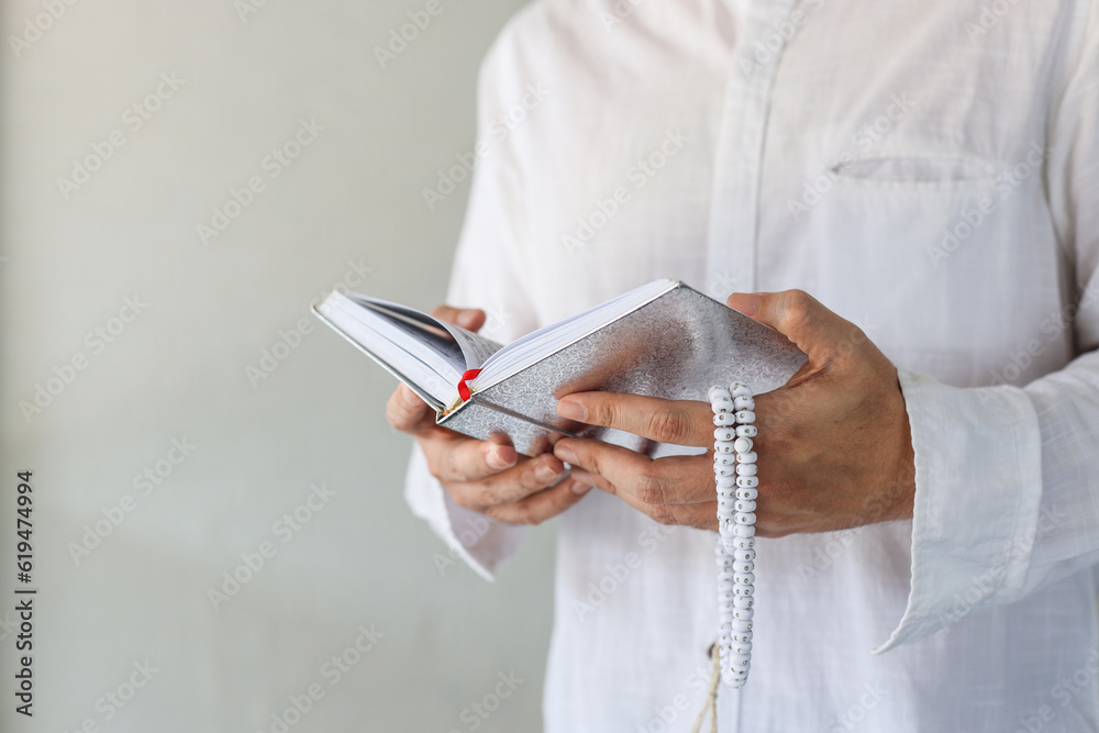 Muslim man holding prayer beads and reading Koran or Quran with copy space