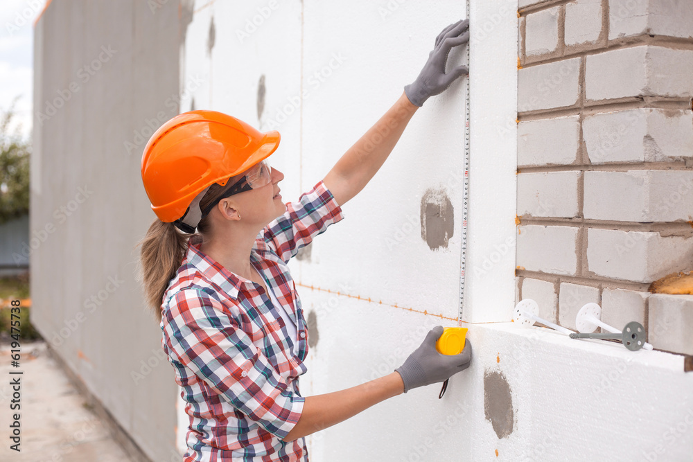 Insulation of the house with polyfoam. The worker is checking with the construction level the accuracy of the installation of polystyrene board on the facade.
