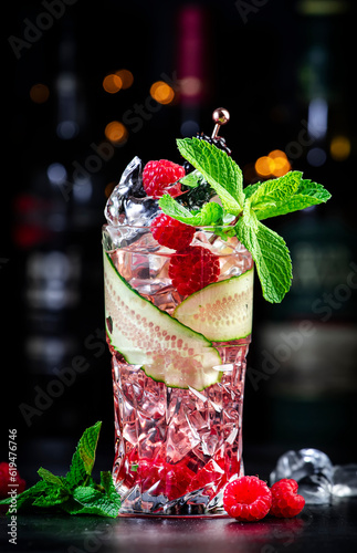 Rose garden alcoholic cocktail drink with dry gin, tonic, rose syrup, lychee juice, lemon, raspberry, cucumber and blackberry with ice. Black bar counter background, bar tools and bottles