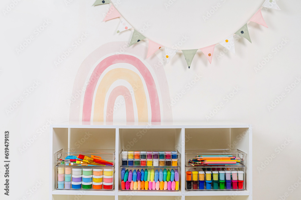 Transparent plastic containers with stationery and supplies for drawing and craft on shelves. White shelving with various material for creativity and art activity. Organizing and storage craft room.