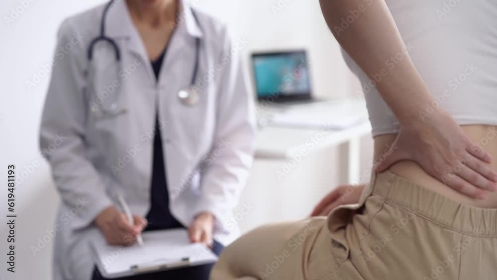 Doctor and patient are in the clinic. Orthopedic in white coat using clipboard for making notes while a woman is rubbing her back, close up. Medicine, physical therapy concept Doctor and patient are in the clinic. Orthopedic in white coat using clipboard for making notes while a woman is rubbing her back, close up. Medicine, physical therapy concept