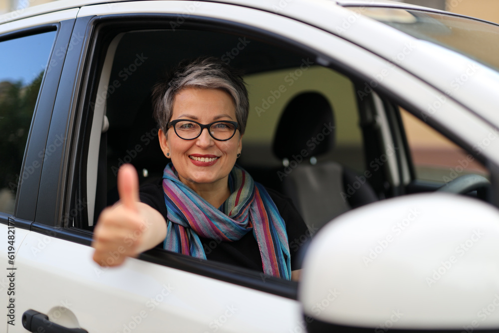 Smiling mature woman showing thumbs up in car driver seat.