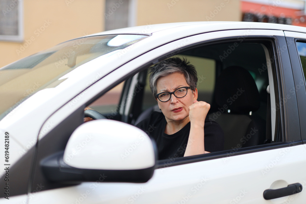 Angry woman shakes her fist while driving a car.