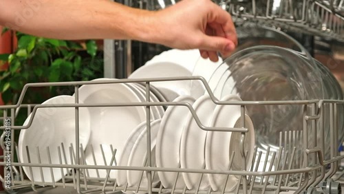 The man pulls out the dishwasher basket and unloads clean plates. Release of the dishwasher after the washing cycle.