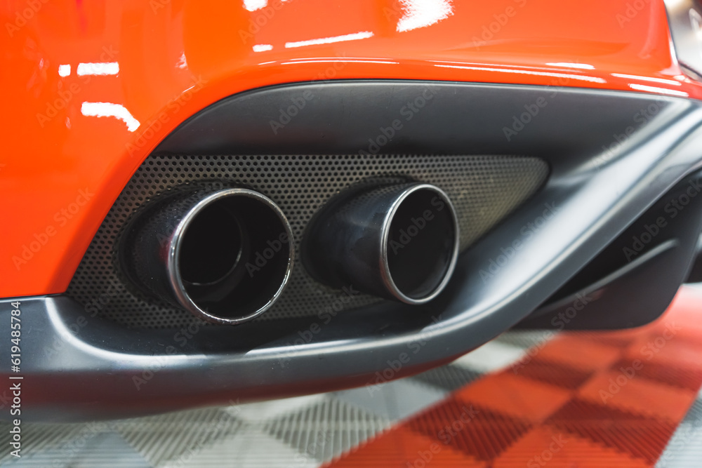 Indoor closeup shot of two exhaust pipes or tailpipes of a fast red sports car. A visit at mechanic's or car detailing studio. High quality photo