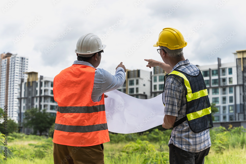 Back view two engineer men holding project blueprint and pointing fingers at high building, Engineer working Outdoor Back view two engineer men holding project blueprint and pointing fingers at high building, Engineer working Outdoor