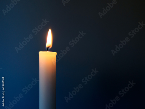 Burning white candle in front of a dark blue background
