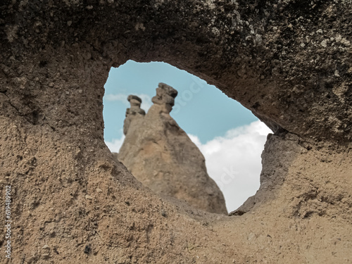  The fairy chimney behind the round cavity in the rock. The natural hole in the rock. Fairy chimneys in Cappadocia. Horizontal photograph.