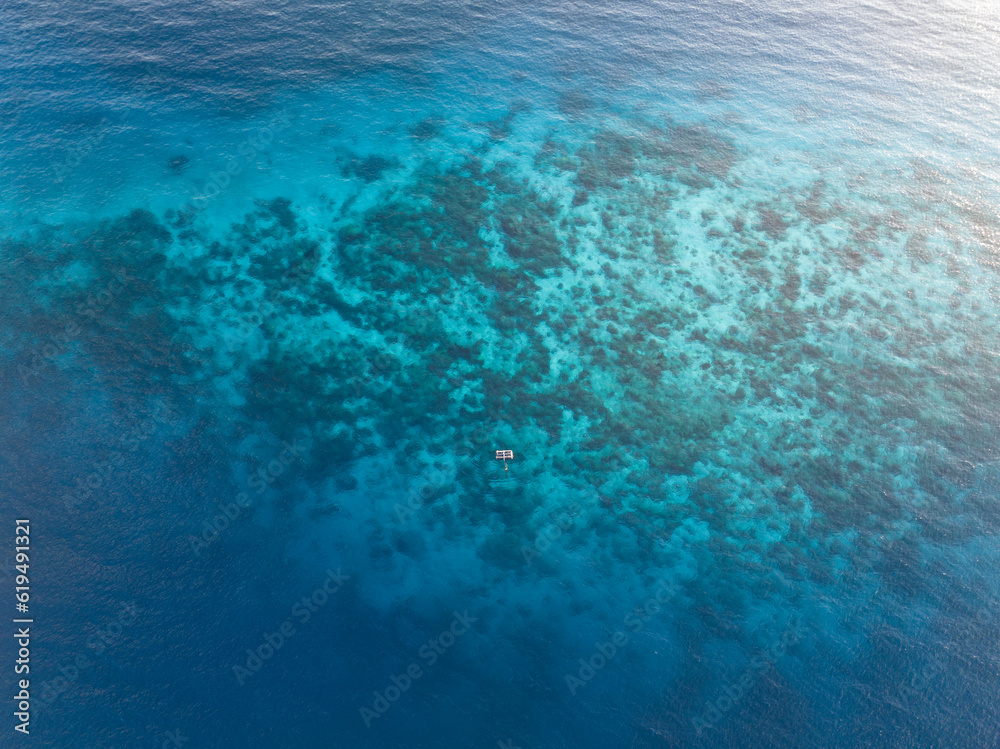 Seen from a bird's eye view, a shallow coral reef is surrounded by clear blue seas in Komodo National Park, Indonesia. This tropical region is known for its high marine biodiversity.