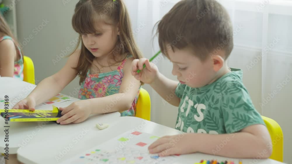 The girl chooses a colored pencil, the boy completes the task. Creative drawing tasks at desks in the first grade. High quality 4k footage The girl chooses a colored pencil, the boy completes the task. Creative drawing tasks at desks in the first grade. High quality 4k footage
