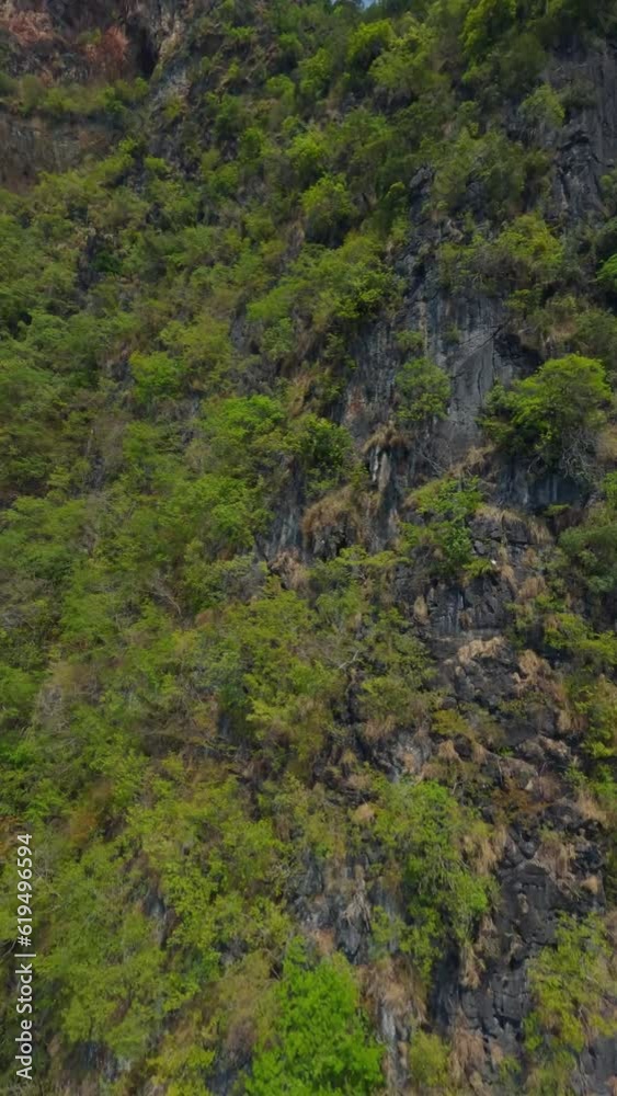 Vertical video. Aerial view climbing up mountain top rock texture with tropical greenery sea ocean landscape. FPV sport drone shot cliff peak with cinematic exotic paradise seascape valley pond cloud Vertical video. Aerial view climbing up mountain top rock texture with tropical greenery sea ocean landscape. FPV sport drone shot cliff peak with cinematic exotic paradise seascape valley pond cloud