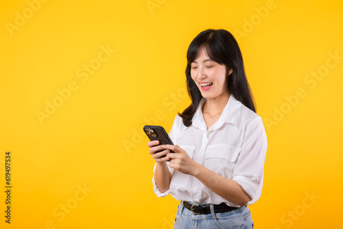 Obraz na plátně Portrait beautiful young asian woman happy smile wearing white shirt and denim plants using smartphone isolated on yellow studio background