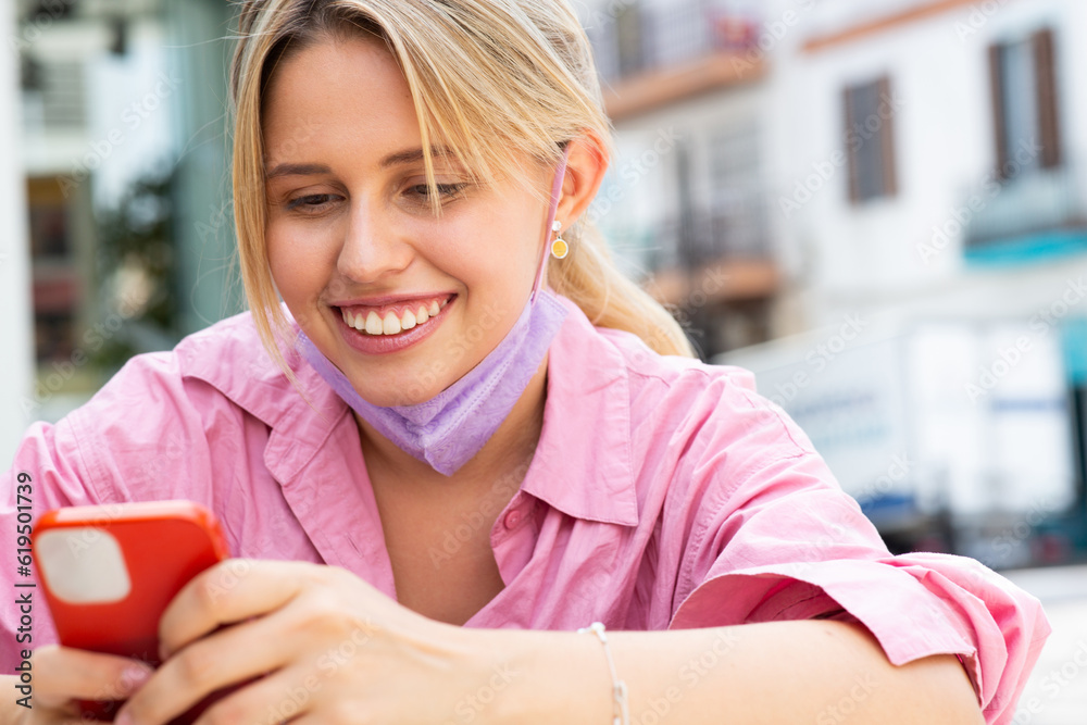 Happy woman texting on mobile phone with mask outside Happy woman texting on mobile phone with mask outside