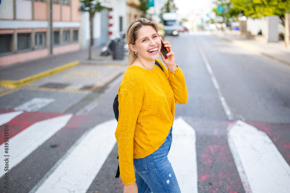 Happy young woman crossing street at cross way talking on phone
