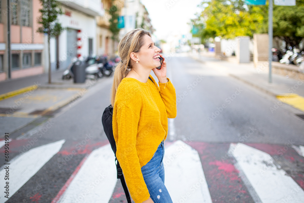 Cheerful young woman crossing street and talking on cellphone Cheerful young woman crossing street and talking on cellphone