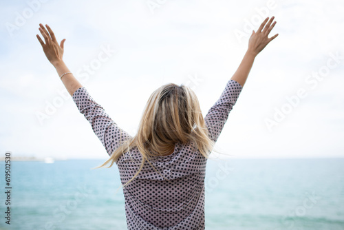 Bilde på lerret Young woman looking at the sea with arms raised