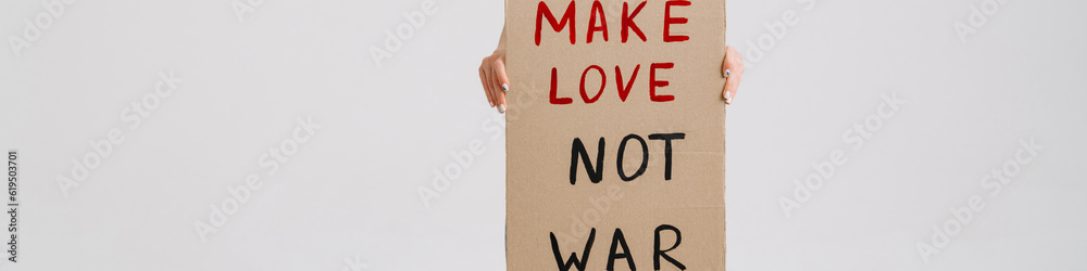 Young woman posing at camera and holding placard with peace message Young woman posing at camera and holding placard with peace message