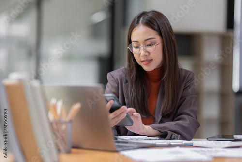  business Asian woman freelancer wear glasses is working her job on phone and laptop in the office. Doing accounting analysis report real estate investment data, Financial and tax systems concept.