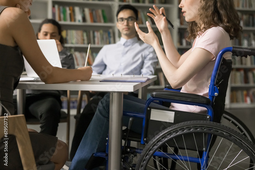 Team of college students and speaker with disability meeting in library, discussing group homework task, class project. Young college girl using wheelchair, talking to classmates. Cropped shot