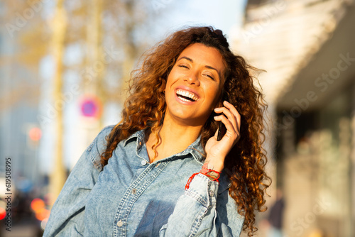Smiling young woman talking on mobile phone walking outdoors in the city