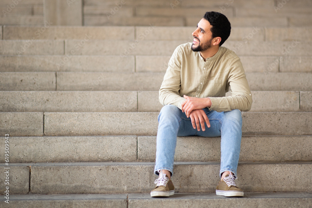 Young man sitting on steps looking away and smiling