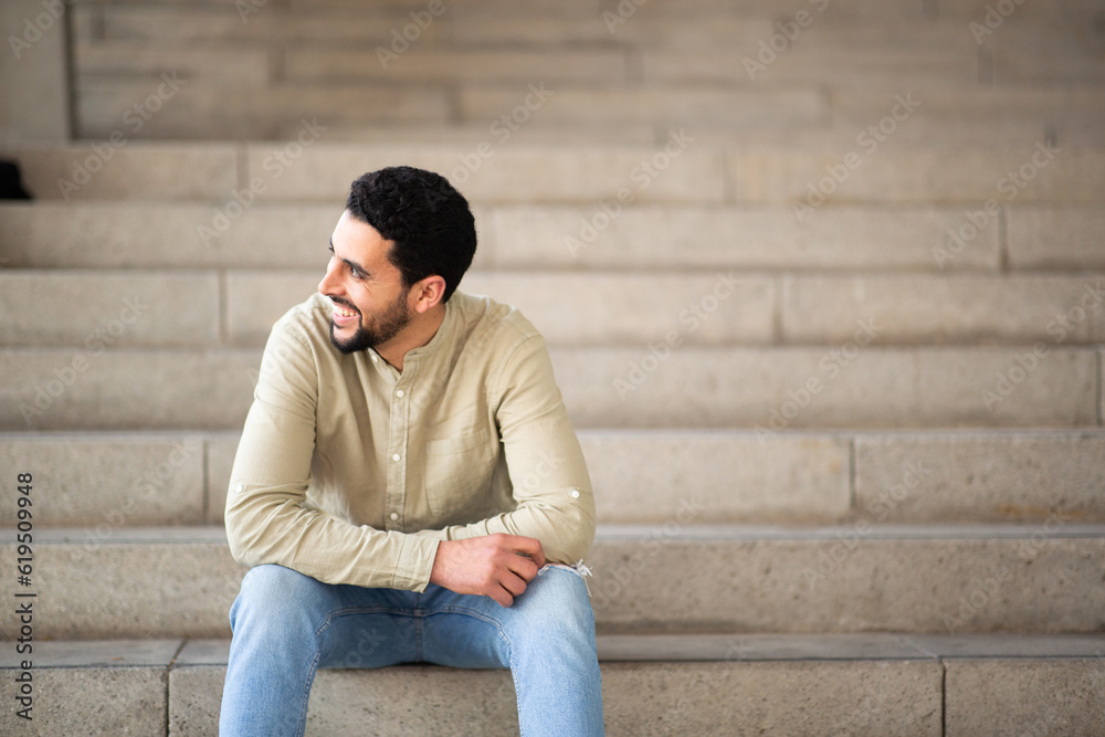 Smiling arabic man sitting on steps looking away Smiling arabic man sitting on steps looking away
