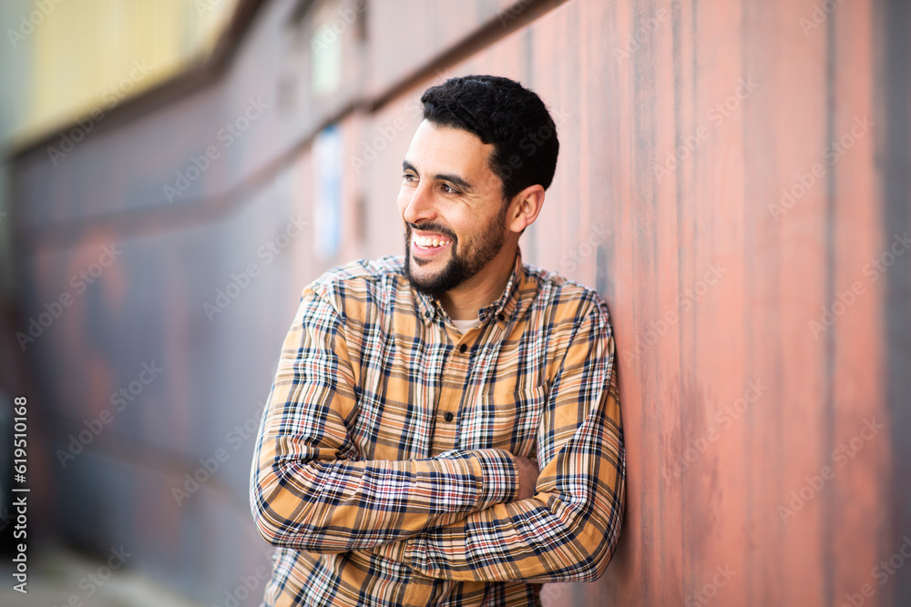 Smiling young arabic man with arms crossed standing against a wall and looking away Smiling young arabic man with arms crossed standing against a wall and looking away