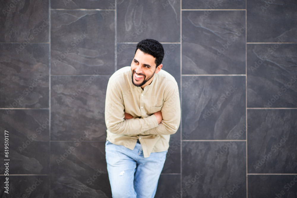 Laughing arabic man leaning against black wall with arms crossed Laughing arabic man leaning against black wall with arms crossed